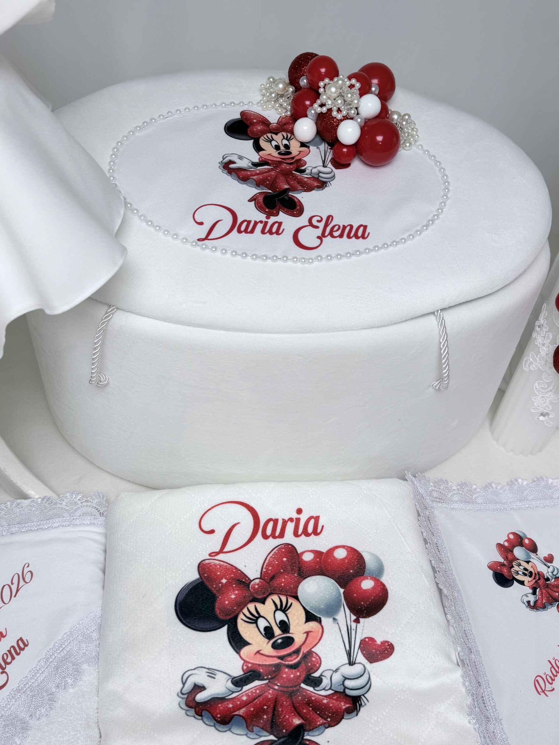 Trusou de botez personalizat pentru fetiță, cu cufăr alb, textile cu Minnie și decorațiuni cu balonașe roșii și albe.
