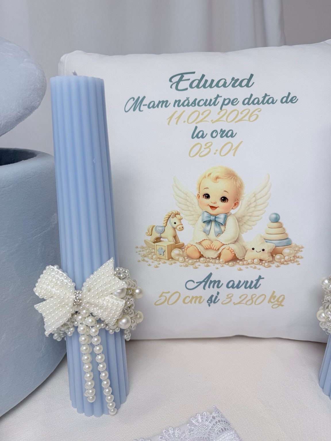 Lumânare bleu cu fundă și șiraguri de perle decorative, lângă perna personalizată cu îngeraș