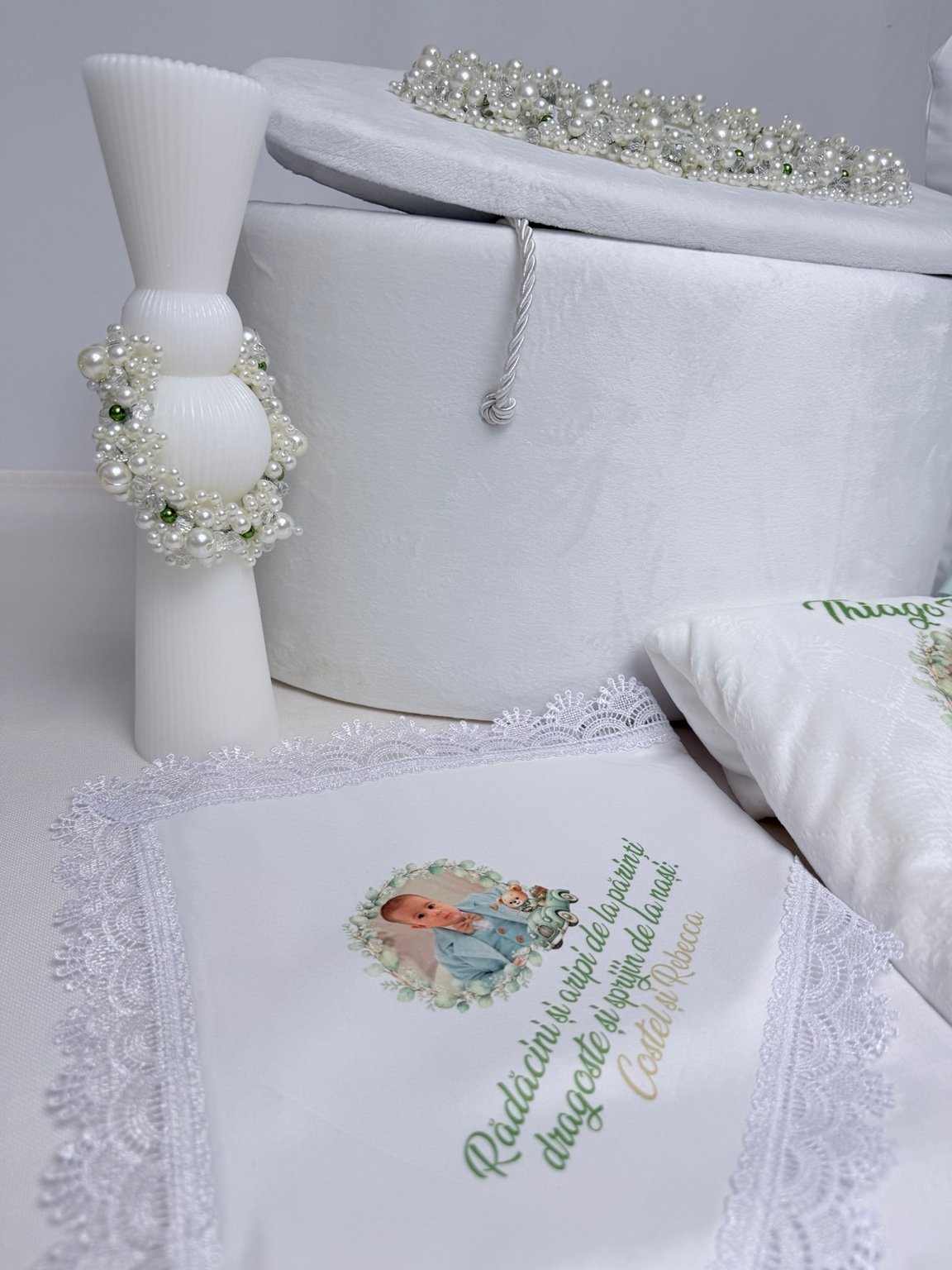 Lumânare albă cu forme rotunjite și ornament din perle, lângă cufărul alb și textilele personalizate