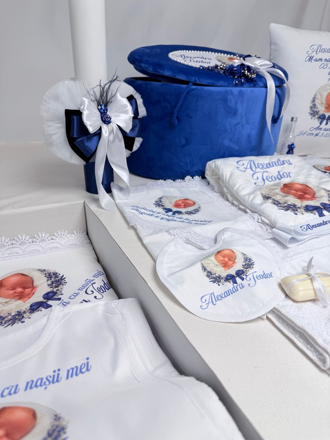 Lumânare albă cu funde albe și albastre, pene decorative și rozetă albă, lângă textilele pentru prima băiță