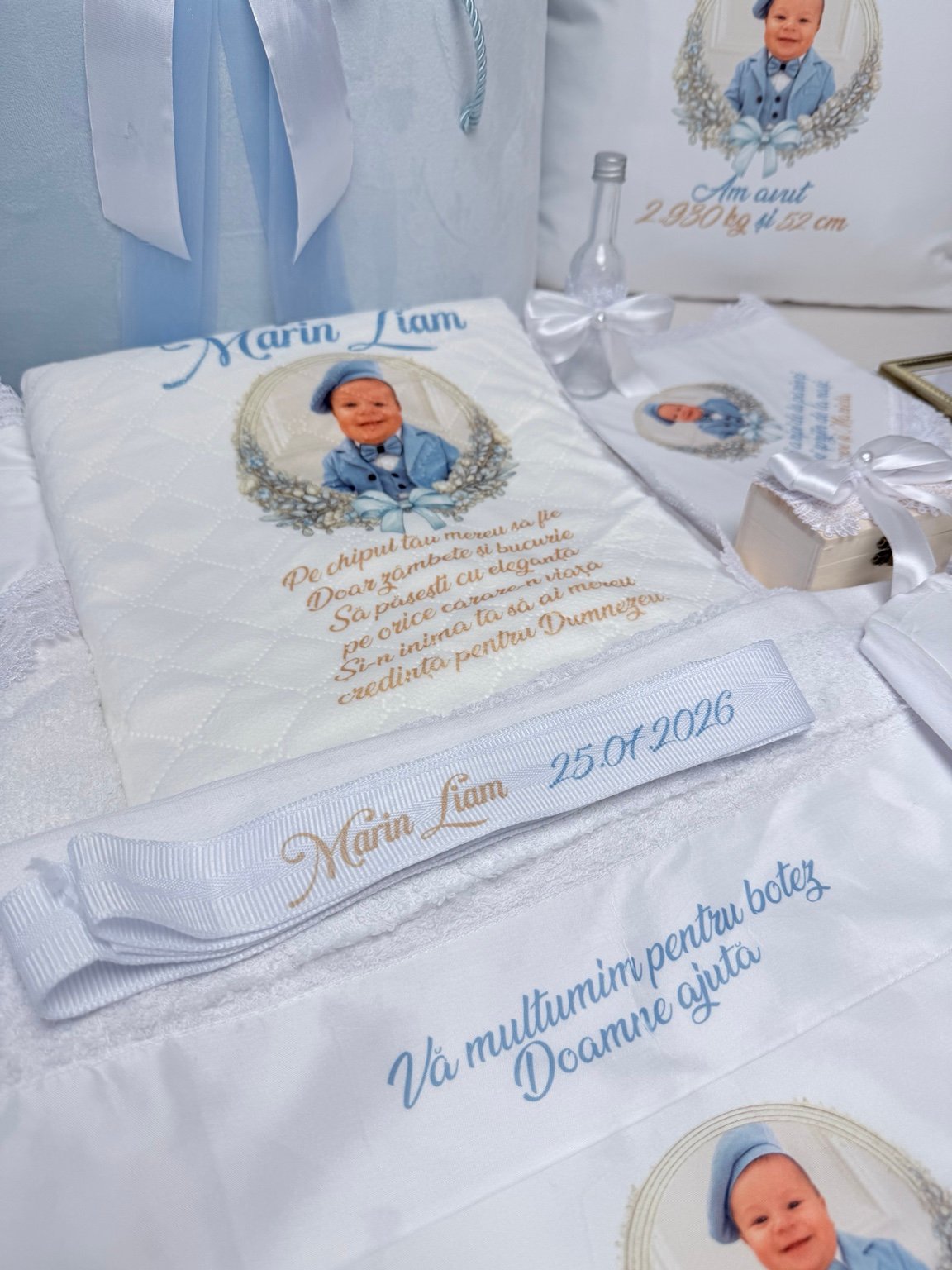 Textile albe cu fotografia bebelușului și mesaje bleu și aurii, alături de fașa personalizată