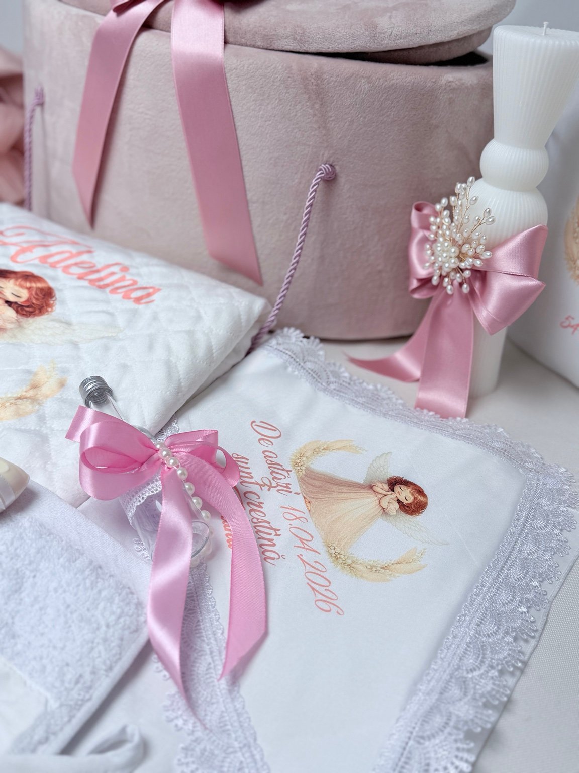 Sticluță pentru mir cu fundă roz și șirag de perle decorative, lângă lumânarea albă și textilul cu îngeraș